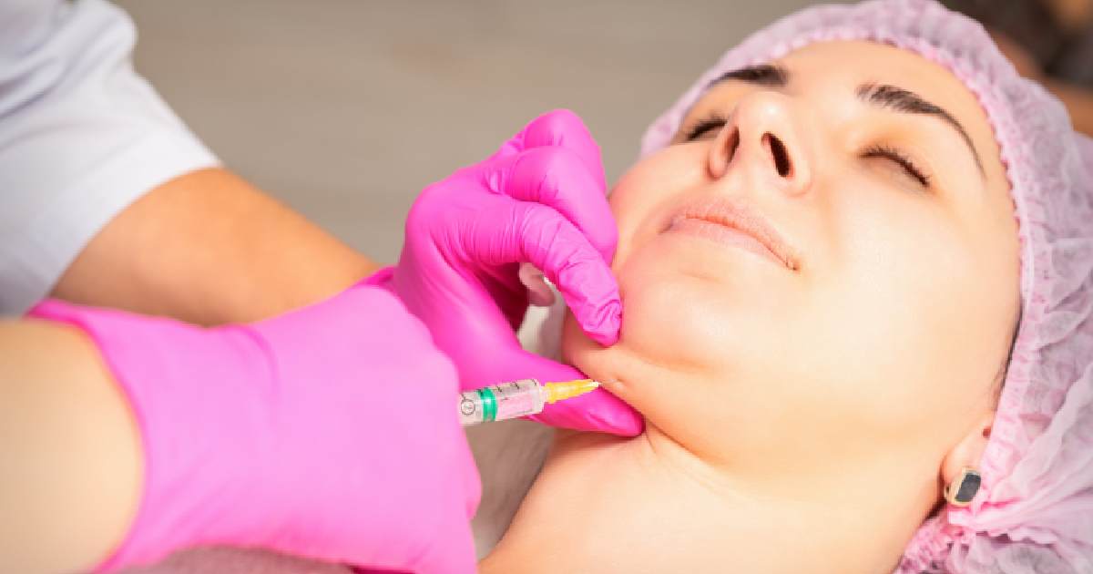 A woman receiving a Kybella injection in the chin area for double chin reduction by a medical professional wearing pink gloves in a clinical setting in Nampa, ID